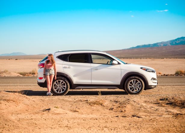 Woman leaning against car standing in the sun